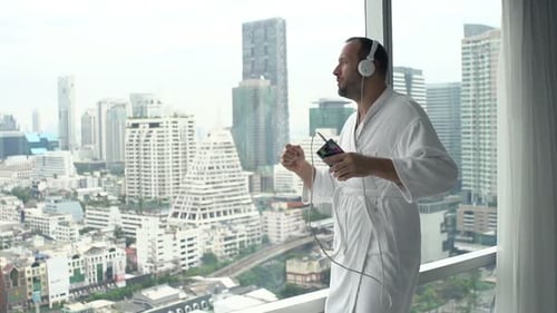 Man in robe listening to music in city apartment