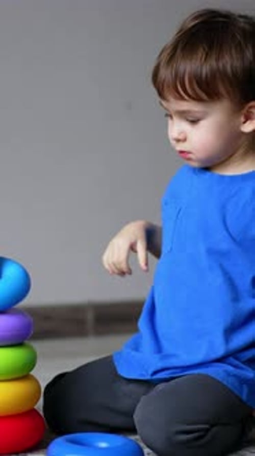 Un niño caucásico sonriente juega con una pirámide de juguete. El niño pone los anillos sobre la base alegremente