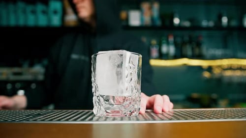 professional bartender stirring ice cubes with a long spoon behind the bar a young man