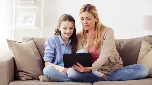 Woman and Girl Using Tablet on Couch at Home