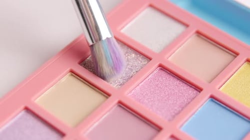 El maquillador recoge el pigmento brillante de la paleta de sombras de ojos de colores brillantes con un pincel