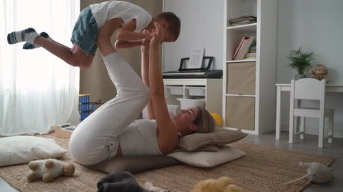 Woman Exercises While Holding Child With Legs Indoors