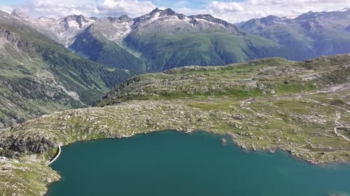 Drone flies over a mountain lake with stunning mountain range in background at Grimselpass, Switzerl