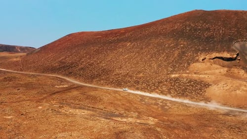 Aerial Shot Following White Car Driving Down a Narrow Path in Red Desert Landscape
