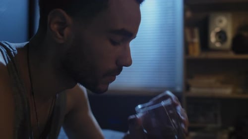 Man Drinks Glass of Liquid in Dark Room