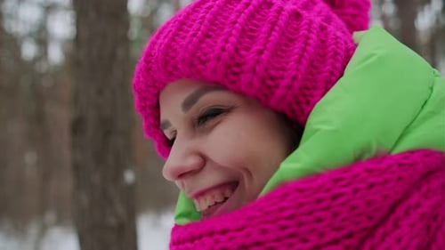 A Beautiful Woman in a Green Jacket Pink Hat and Scarf Smiles Standing in a Winter Forest