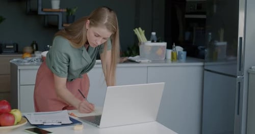 Woman Working at Home in Kitchen with Laptop