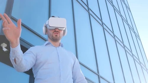 A Man Wearing a Virtual Reality Helmet is Standing in Front of a Building Looking Up at the Sky