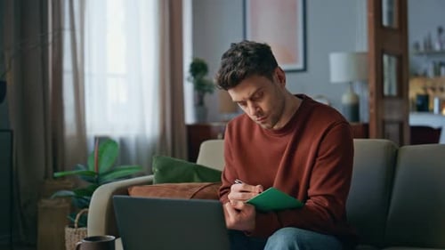 Young Adult Works at Home with Laptop and Notebook