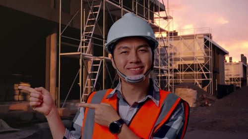 Close Up Of Asian Male Engineer Smiling And Pointing To Side At Building Site