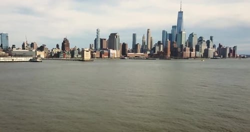Slow upward tilting drone shot of the Hudson River and New York City skyline as a boat passes.