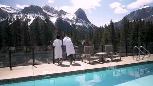 Couple in robes hugging at luxury hotel pool overlooking snow capped mountains in Canada