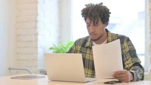 Young Adult Working at Laptop and Reading Documents