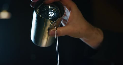 Close up of a professional bartender is preparing an alcoholic cocktail with ice cubes to customer
