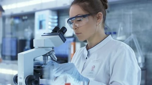 Medical Research Scientists putting Slides in Place and Looking at Samples Under Microscope. She Wo