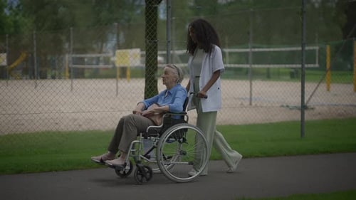 Woman Pushes Senior in Wheelchair Through City Park