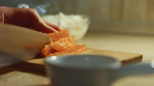 Closeup of Female Hand Slicing Fresh Salmon Fillet on a Wooden Board