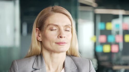 Close up of a businesswoman in a suit relaxing with her eyes closed while sitting at a workplace