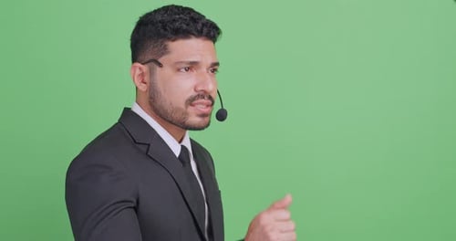 Young male economist wearing a microphone is explaining something. Isolated on green background