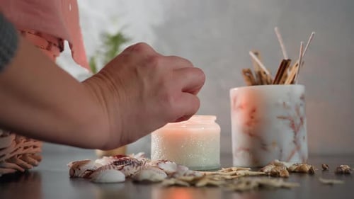 Hand Lighting Candle with Matchstick on Marble Table with Seashell Decor