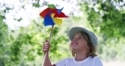 in a day of sun and wind, a happy little beautiful girl in green nature blows on a colorful pinwh