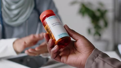Hand of Unrecognizable Patient Holding Jar of Prescription Medicine in Clinic