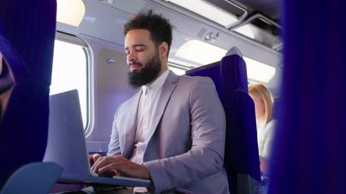 Ein Geschäftsmann mit Bart arbeitet fleißig an seinem Laptop, während er in einem Zug reist
