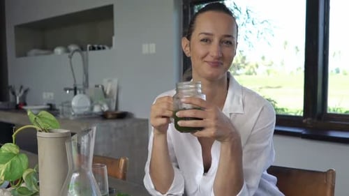 Woman Drinking Green Smoothie in Bright Modern Kitchen