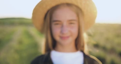 Close up. Little girl with hat looking at camera against the background of rapeseed field at organic