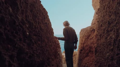 A câmera fica atrás de uma mulher loira viajante. Ela está explorando falésias incríveis em Portugal.