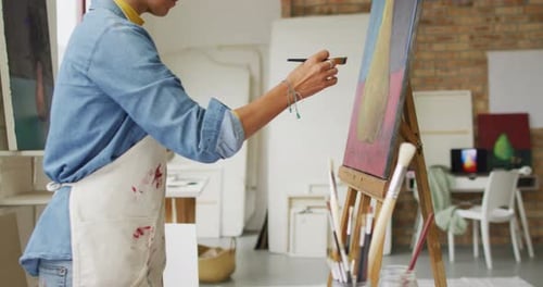 Video of biracial female artist painting in studio