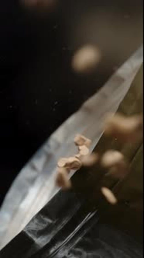 Vertical video. Soluble coffee granules slowly fall from the packet, filling the entire frame.