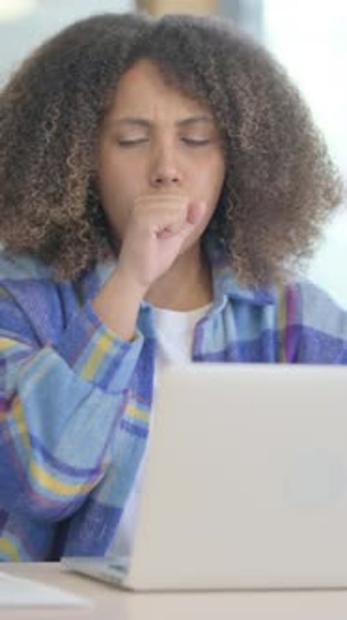 Young Woman Coughing while Working on Laptop