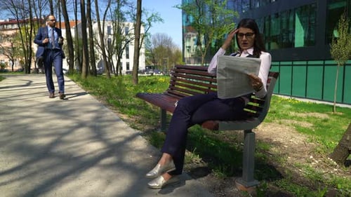 Young Attractive Businesswoman Reading Newspaper on Bench in the City 40s