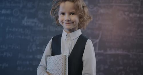 Smiling Child with Notebook in Front of Chalkboard
