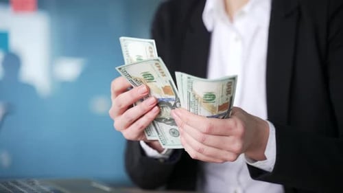 Professional woman in business attire counting money at desk. Close up of hands holding hundred