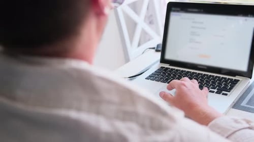 Freelancer trabaja en la computadora portátil y bebe mientras está sentado frente a la ventana en el escritorio