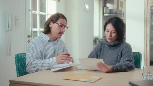 Man and Woman Discuss Documents at Table Indoors