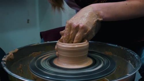 Potter working on potters wheel making ceramic pot from clay in pottery workshop.