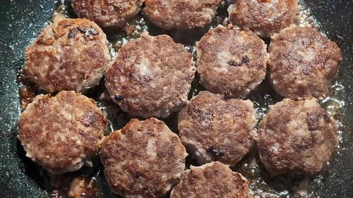 Fleischbällchen, die in Butter in einer schwarzen Pfanne gebraten werden, während das Sonnenlicht reflektiert wird. Nahaufnahme