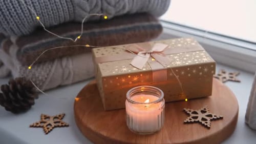 Burning Candle with Christmas Gift and Cozy Sweaters