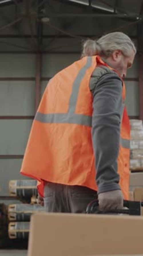 Warehouse Worker Pulling Hand Pallet Truck with Boxes in Storage Office