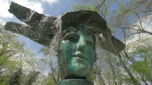 Camera zooms to running water jets from bronze mask fountain, slow motion