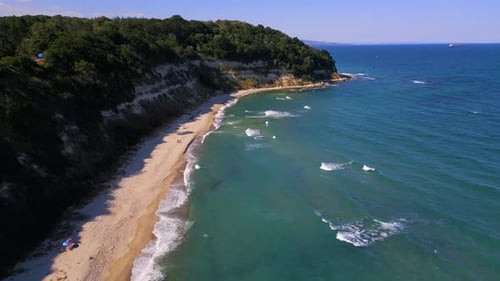 Aerial footage of a scenic sandy beach with waves gently hitting the shore, people relaxing under um