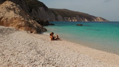 Mujer leyendo un libro en una playa de guijarros durante un cálido día de verano en Cefalonia, Grecia