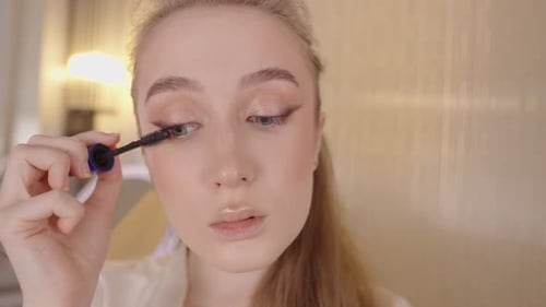 Close Up View of an Attractive Young Woman Carefully Applying Black Mascara to Her Eyelashes with a