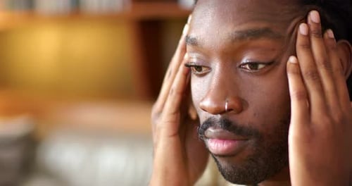 African American man feeling tension, pressing temples and rubbing forehead on couch, nose ring