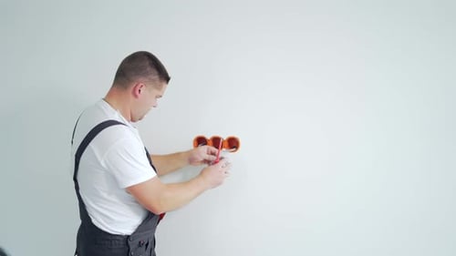 Male worker professional qualified electrician installs electrical outlet in apartment after repair.