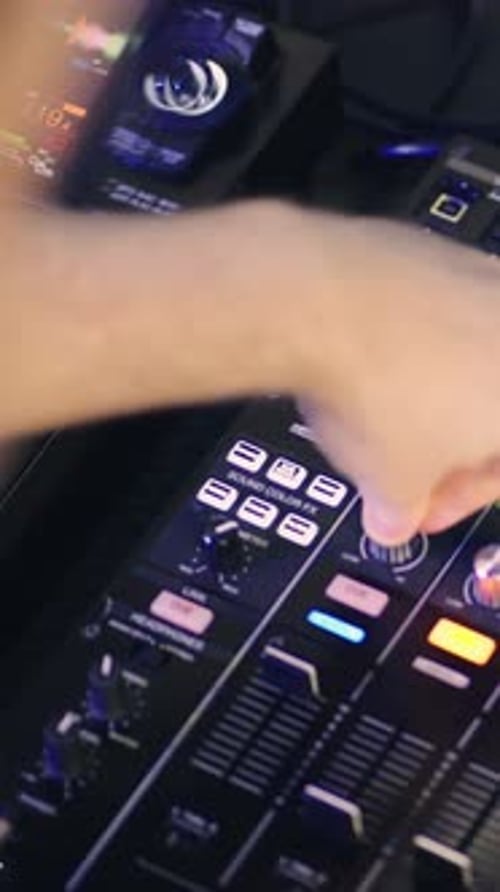 Closeup of DJ Adjusting Knobs and Faders on Illuminated Audio Mixer Console Manipulating Sound