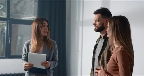 Un joven y una mujer felices hablan con una hermosa agente inmobiliaria en una habitación espaciosa y luminosa en busca de una nueva